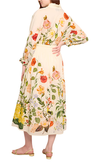 A person in the Louisa Dress by Cara Cara, featuring a floral print and ruffled neckline, stands with their back turned, wearing sandals.