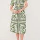 A person wears the Cara Cara Malena Dress—a green and white patterned, belted short-sleeve dress—with beige heeled sandals, standing against a plain light background.
