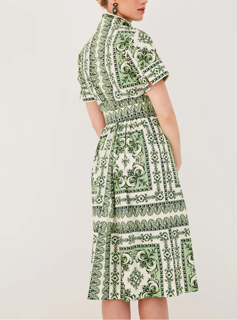 A woman is seen from the back wearing the Cara Cara Malena Dress, a green and white patterned short-sleeve dress with a belted, fitted waist, set against a plain background.