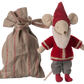 The Maileg Santa Mouse wears a red hat, red sweater, gray pants, and red shoes, and stands beside a tied beige and red striped fabric bag.