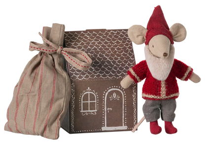 The Maileg Santa Mouse wears a red outfit and hat, standing beside a striped cloth bag and a cardboard Mouse Gingerbread House featuring white door and window designs.