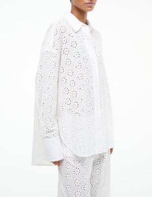 Model wears the Staud Colton Top, a cotton eyelet design with an oversized fit, paired with matching pants. Shown from the waist up against a plain background.