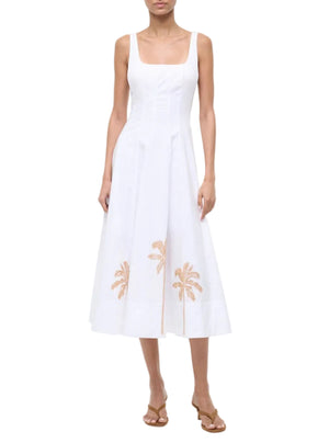 A woman wears the Staud Wells Palm Embroidery Dress, a sleeveless white cotton poplin midi with a fitted waist, square neckline, and palm tree embroidery near the hem, paired with tan heeled sandals.