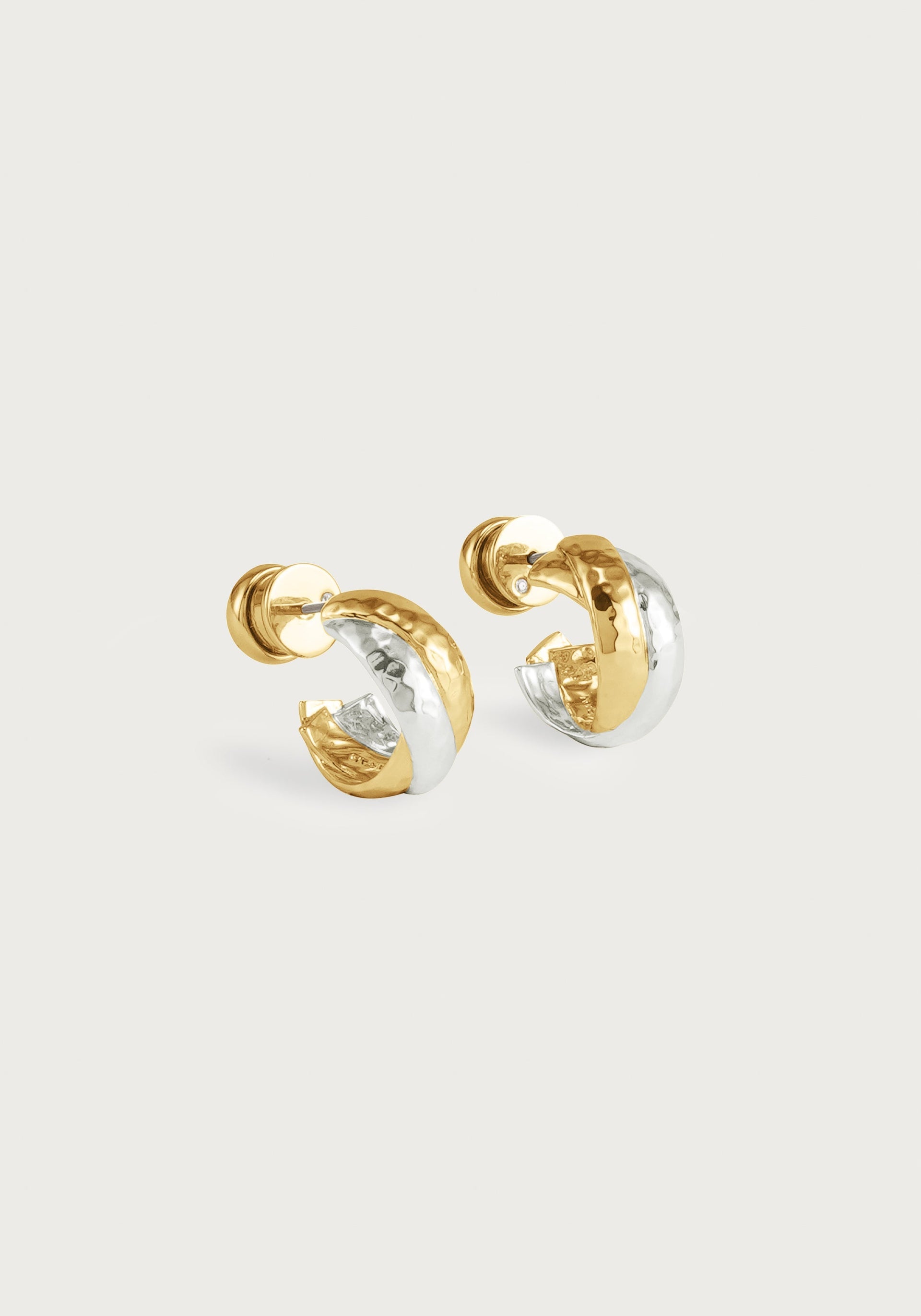 The Anabel Aram Farrier Triple Huggie Hoop Earrings feature small, rounded hoops with a hammered texture and alternating gold and silver segments, creating a striking mixed metal look against a plain white background.