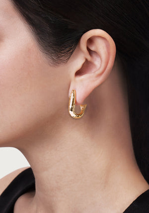 Anabel Aram Milos Fish Hoop Earrings, shaped like a fish and crafted in 18K gold plate, worn in an earlobe.
