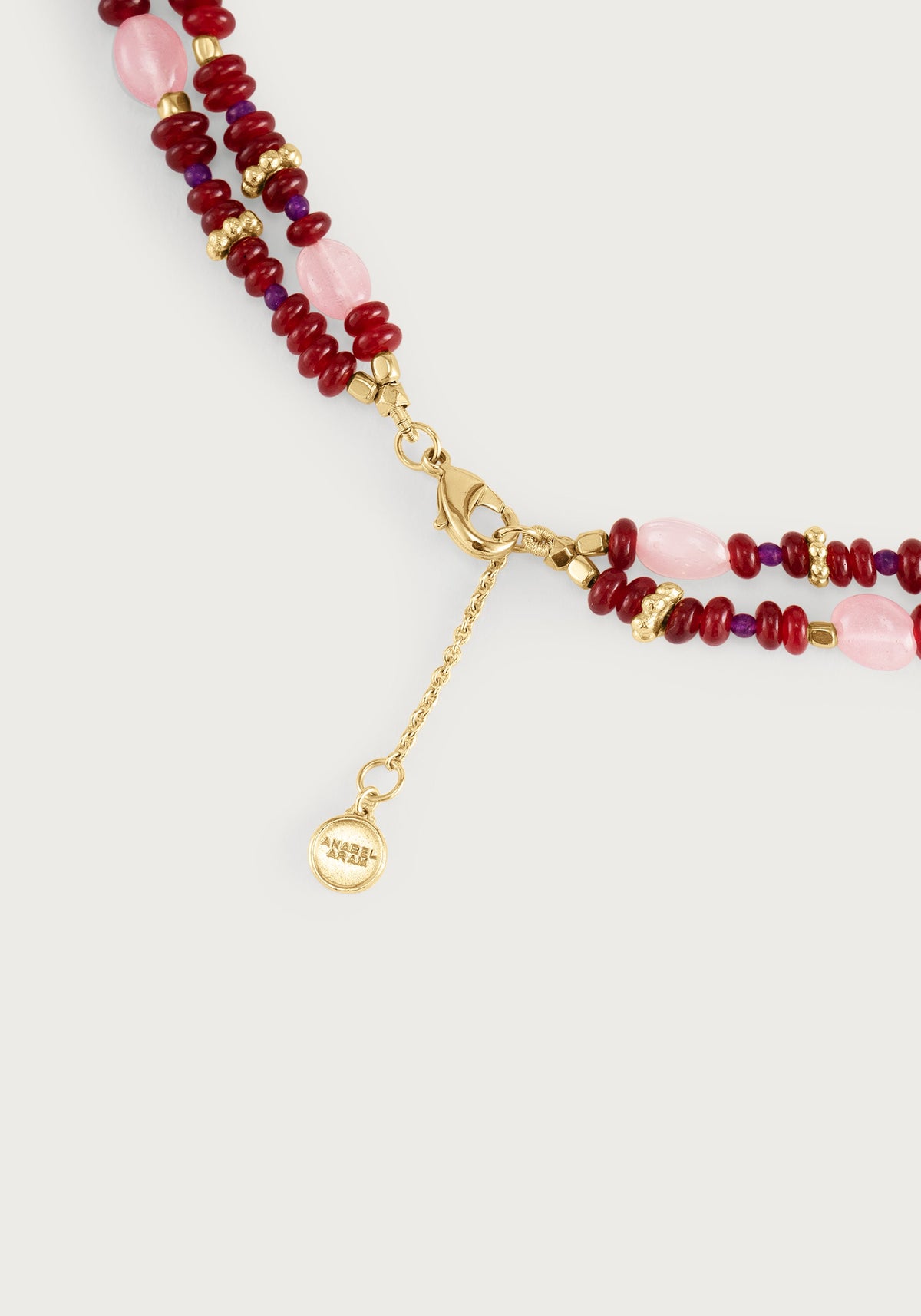 Anabel Aram Milos Beaded Necklace featuring double strands of red, purple, and light pink beads with gold-tone spacers, a lobster clasp, a branded charm, and lapis lazuli and turquoise accents.