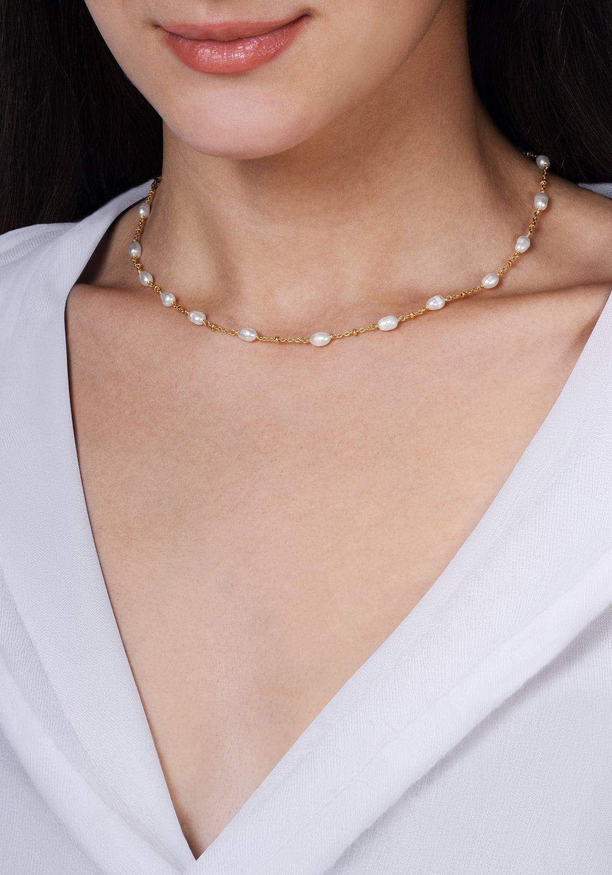 Anabel Aram Milos Multi Beaded Necklace featuring small, evenly spaced white pearls on an 18k gold plated chain worn around the neck.