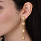 Anabel Aram Milos Soleil drop earrings in 18K gold plate, featuring a vertical row of four sun-shaped charms with inlaid circular stones, worn on an earlobe.