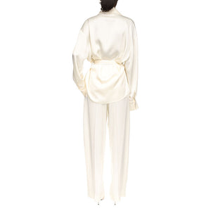 Person wearing a Victoria Beckham Pyjama Wrap Blouse in ivory crepe back satin with matching wide-leg pants, both featuring relaxed tailoring, shown from the back against a white background.