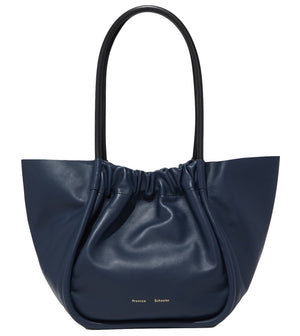 Proenza Schouler's Large Ruched Tote in navy blue leather showcases a ruched top, dual black handles, and a subtle logo stamp on the front, adding elegance to this stylish accessory.