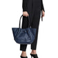 Woman holding a Proenza Schouler Large Ruched Tote bag and wearing a black belt, pants, and heeled shoes, cropped at the waist.