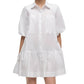 A woman wears the Simkhai Crissy Dress, a casual white mini dress featuring shirting inspiration, puffed sleeves, front pockets, and a gathered skirt.