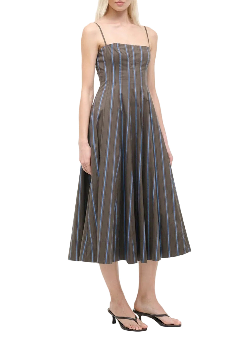 A woman wears the Staud Wylie Dress—a sleeveless, corset-style cotton poplin midi with blue vertical stripes and thin straps from Staud—paired with black heeled sandals.