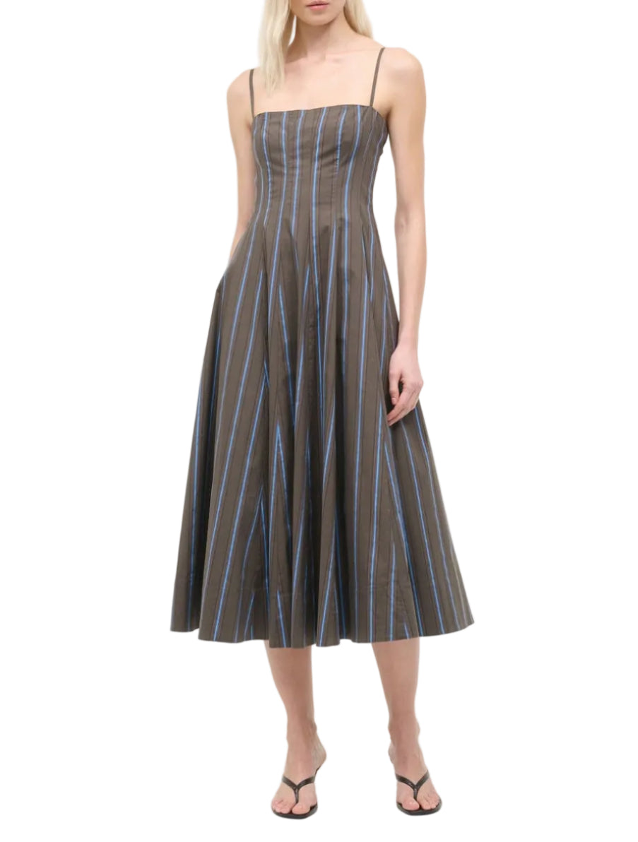A woman wearing a Staud Wylie Dress, a sleeveless brown cotton poplin midi dress with blue vertical stripes and spaghetti straps by Staud, paired with black sandals.