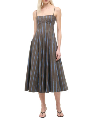 A woman wearing a Staud Wylie Dress, a sleeveless brown cotton poplin midi dress with blue vertical stripes and spaghetti straps by Staud, paired with black sandals.