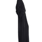 A woman, standing in profile against a white background, wears CO's Wide Leg Crepe Pant as part of a loose-fitting black ensemble with long sleeves.