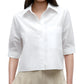 A woman wears the TWP Short Lived Top—a white, boxy fit, short-sleeved cotton poplin button-up shirt with a chest pocket—paired with beige pleated pants, shown from shoulders to hips.