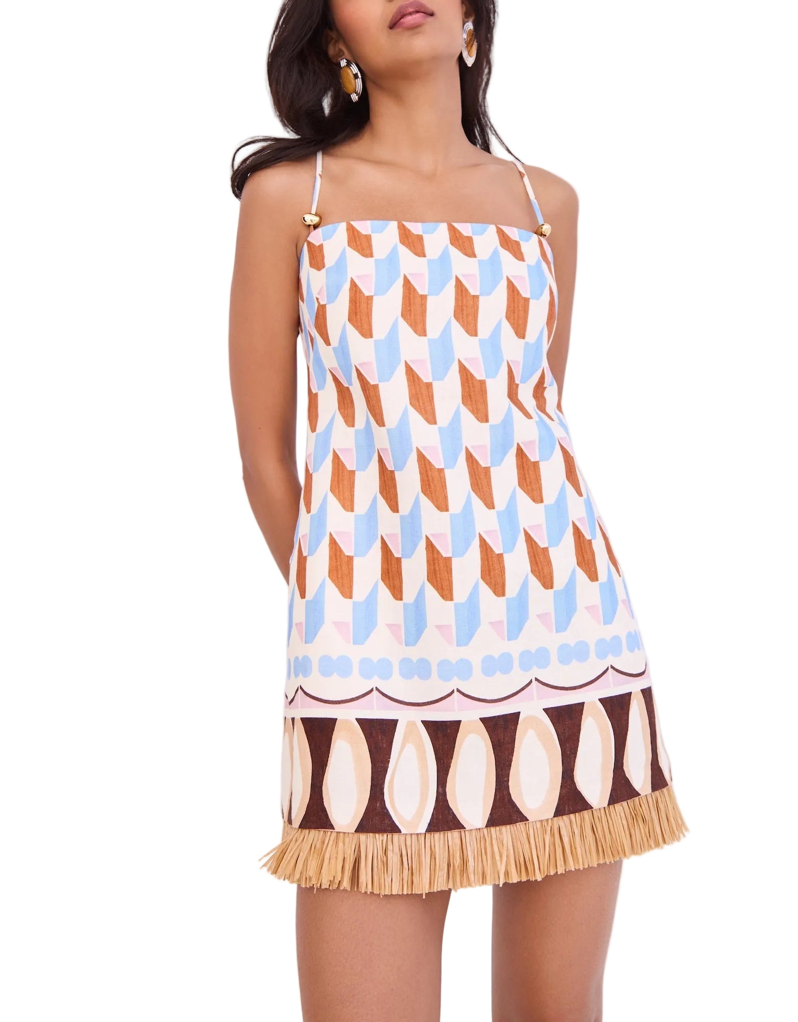 A woman wears the Cara Cara Valencia Mini Dress, a sleeveless shift mini with thin straps, geometric patterns in brown, blue, and tan, and raffia fringe at the hem.