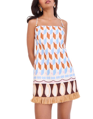 A woman wears the Cara Cara Valencia Mini Dress, a sleeveless shift mini with thin straps, geometric patterns in brown, blue, and tan, and raffia fringe at the hem.