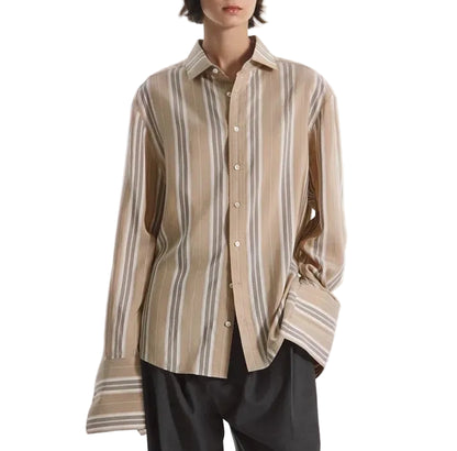 A person wearing the CO Standing Collar Silk Shirt, an oversized beige and white striped button-down with long sleeves and horn buttons, paired with dark pants and standing against a white background.