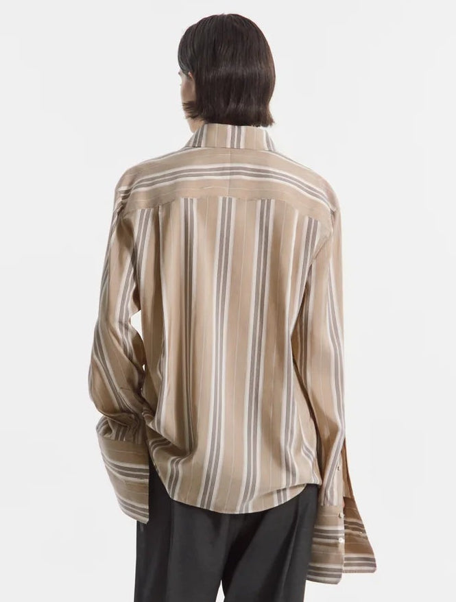 A person is seen from the back against a plain white background, wearing CO’s Standing Collar Silk Shirt—an oversized, long-sleeve button-down featuring loose beige and white vertical stripes and subtle horn button detailing.