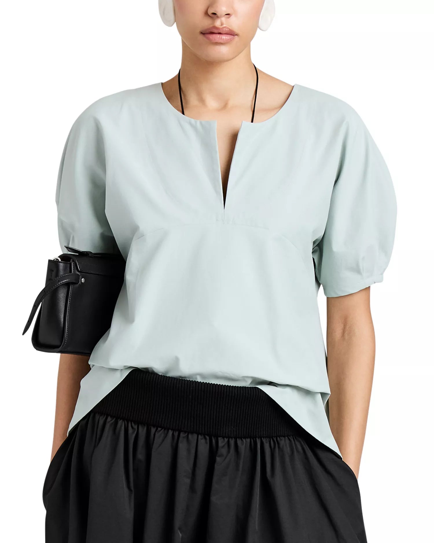 Someone wearing a light blue Proenza Schouler White Label Tia Top with a front slit neckline, paired with a black skirt and carrying a small black bag under their arm.