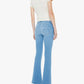 A person wearing a white short-sleeve top, The Weekender Fray light blue mid-rise flare jeans from Mother crafted from recycled stretch denim with raw hems, and silver high heels, stands with their back to the camera against a plain white background.