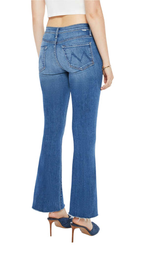 In Los Angeles, someone walks away wearing the Mother Denim The Weekender Fray mid-rise flare jeans in stretch denim, paired with a white top and matching high-heeled shoes. The blue jeans feature stitched back pockets.