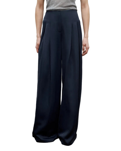 A person wears the TWP Drew Coated Viscose Linen Pant, featuring a high-rise wide leg fit with front pleats, paired with a light grey top.
