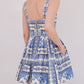 A woman stands facing away, wearing the Cara Cara Micaela Mini Dress—a blue and white patterned fit-and-flare style with a structured bodice, square back, and visible zipper.