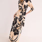 A woman wears the Cara Cara Montgomery Silk Midi Dress, a long-sleeved hammered silk piece featuring an allover beige and black floral print, standing against a plain light background.