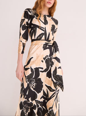 A person wears the Cara Cara Montgomery Silk Midi Dress in beige hammered silk with a bold black floral print and matching belt, standing against a plain light background.