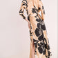 A woman models the Cara Cara Montgomery Silk Midi Dress, featuring hammered beige silk with an allover black floral print and a slit, set against a plain light background.