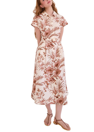 A woman wears the Cara Cara Sawyer Dress, a light-colored, short-sleeved collared shirtdress with a brown floral print, paired with beige sandals.