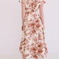 A woman faces away, wearing the Cara Cara Sawyer Dress—a cream belted A-line with short sleeves and a brown floral and leaf print—paired with flat sandals.