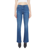 A person wears The Weekender by Mother—blue bootcut flare stretch denim jeans—with black pointed shoes and a white cropped top; jeans are shown from the front.