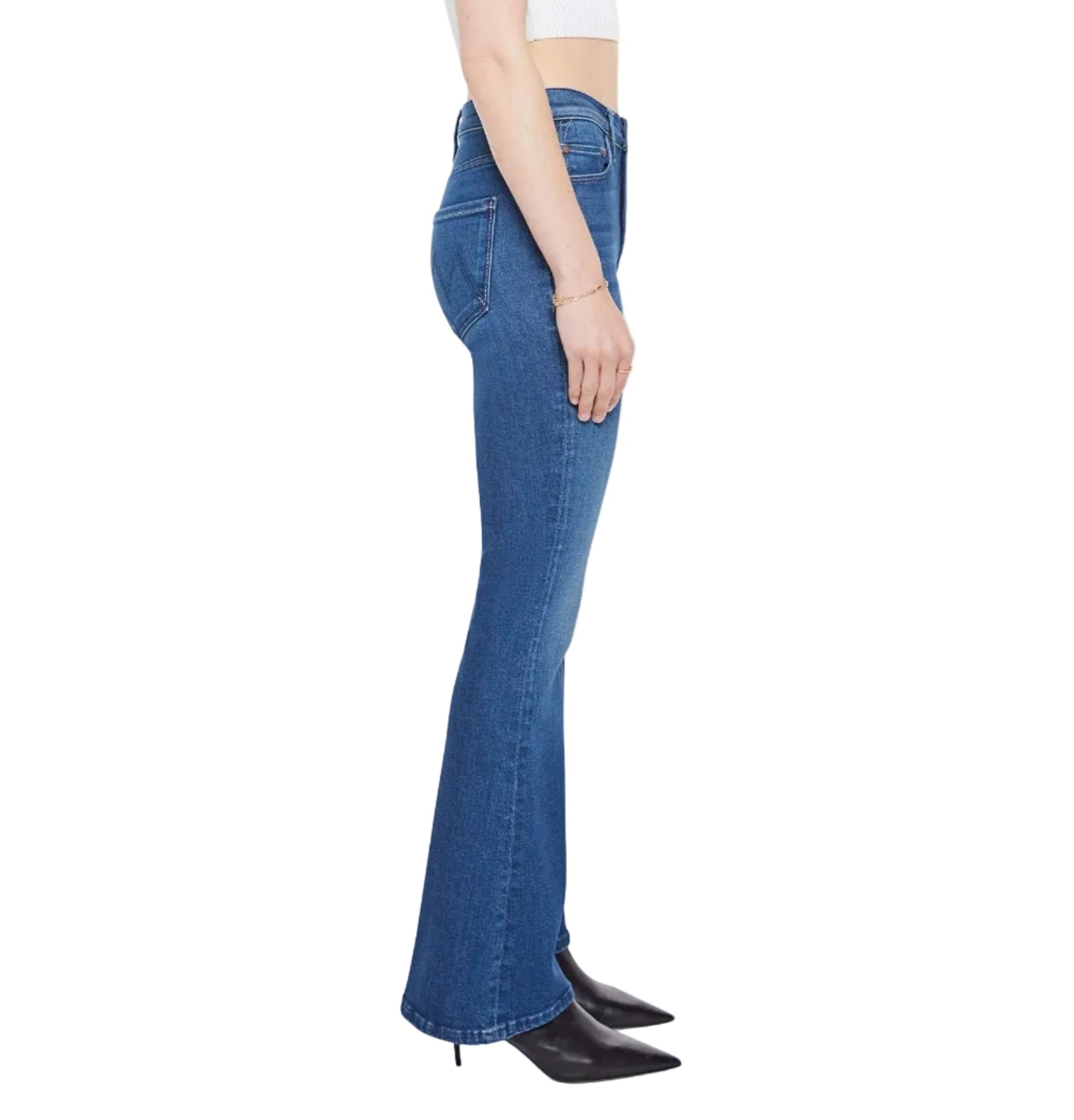 A person stands sideways against a white background wearing Mother’s The Weekender mid-rise blue bootcut stretch denim jeans, a white sleeveless top, and black pointed-toe heeled boots.