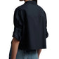 Someone wearing the TWP Next Ex Shirt, a black, long-sleeve cropped top with a boxy silhouette and rolled-up sleeves, is seen from behind paired with blue jeans.