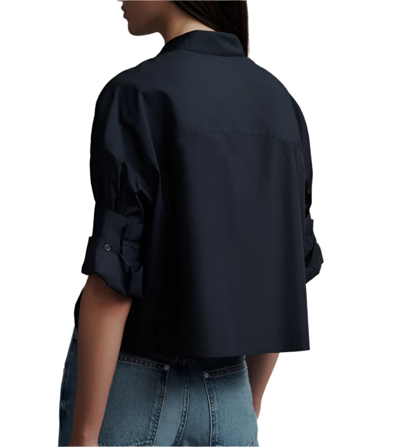 Someone wearing the TWP Next Ex Shirt, a black, long-sleeve cropped top with a boxy silhouette and rolled-up sleeves, is seen from behind paired with blue jeans.