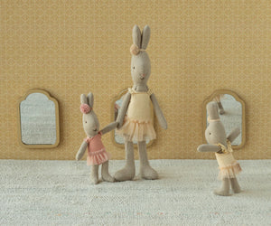 Three Maileg "Rabbit, Micro - Ballet Suit & Skirt Rose" figures pose gracefully like ballet dancers, dressed in rose ballet suits and skirts, standing before a patterned wall with three small mirrors.