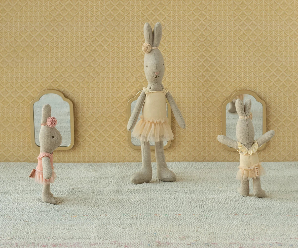 Three Maileg Rabbit Size 1, Classic - Ballet Suit and Skirt Cream dolls stand in front of small mirrors against a patterned wall and light-colored floor, dressed in ballet costumes with delicate tulle skirts, ready to dance gracefully.