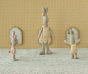 Three Maileg Rabbit Size 1, Classic - Ballet Suit and Skirt Cream dolls stand in front of small mirrors against a patterned wall and light-colored floor, dressed in ballet costumes with delicate tulle skirts, ready to dance gracefully.