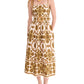 A woman wears the Cara Cara Lee Midi Dress—a sleeveless white fit-and-flare midi with gold floral patterns, removable belt, and pockets—styled with gold sandals and jewelry.