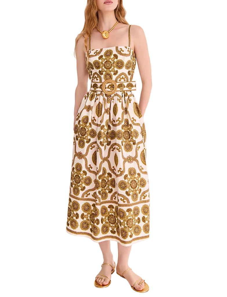 A woman wears the Cara Cara Lee Midi Dress—a sleeveless white fit-and-flare midi with gold floral patterns, removable belt, and pockets—styled with gold sandals and jewelry.