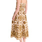 A woman, barefoot and angled away, models the Cara Cara Lee Midi Dress—a sleeveless, fit-and-flare ankle-length dress adorned with gold floral patterns.