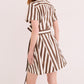 A woman wears the Cara Cara Lagos Dress, a short-sleeved mini shirt dress with brown and white stripes and a collared neckline, standing with her back turned and slightly to the side.