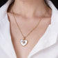 A person wears a gold chain necklace featuring an Anabel Aram Heart Radiant Charm with a white inlay and a smaller central gold heart.