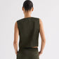 A person stands facing away, wearing the TWP High Neck Hidden Placket Vest in olive green with wide-leg pants that have asymmetric detailing, set against a plain light background.