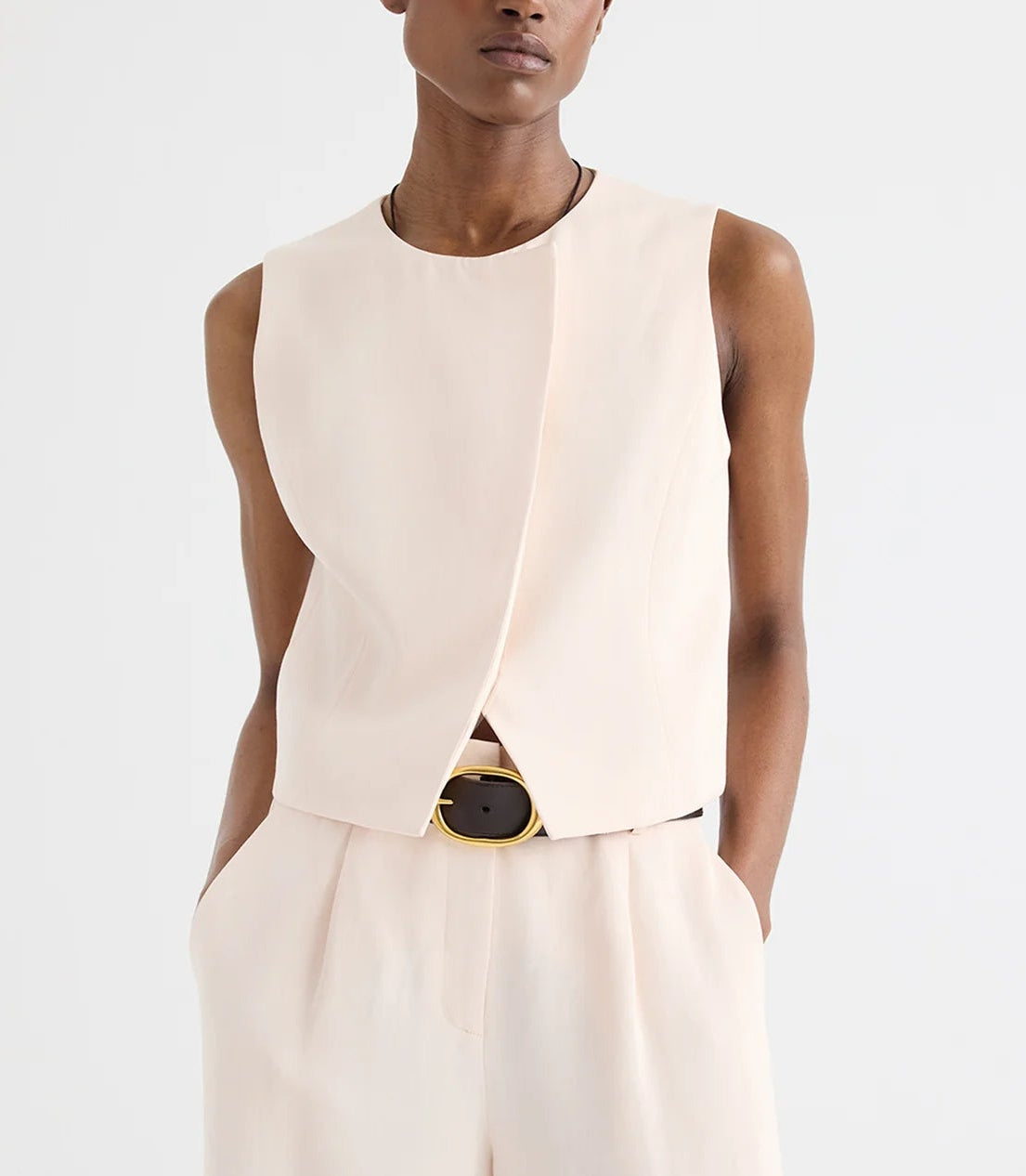 A person wears the TWP High Neck Hidden Placket Vest in sleeveless light beige, paired with matching high-waisted pants made from coated viscose linen, standing against a plain white background.