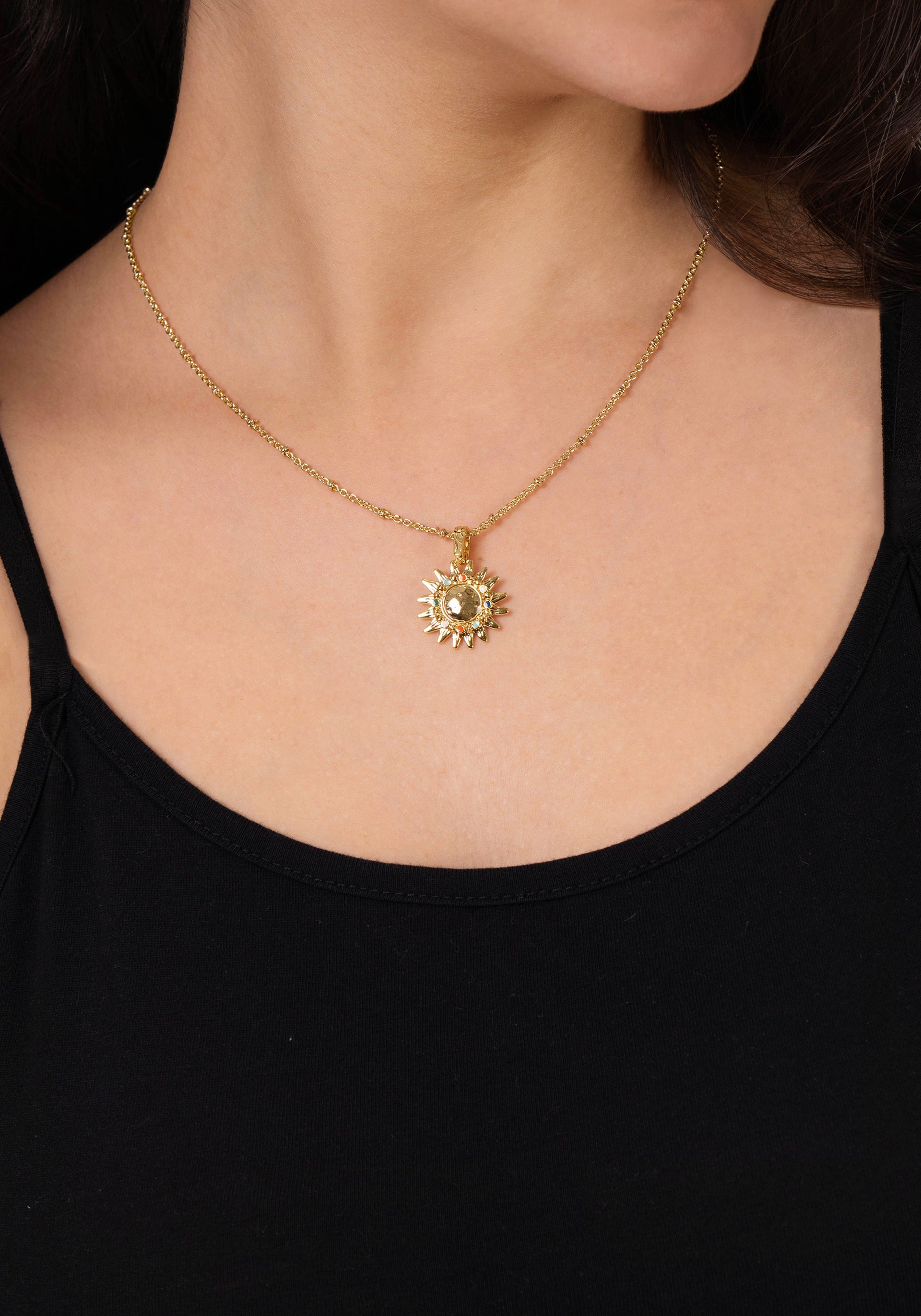 A woman wearing a black top and the Anabel Aram Milos Soleil Charm, a striking gold sunburst necklace inspired by the Mediterranean sun.